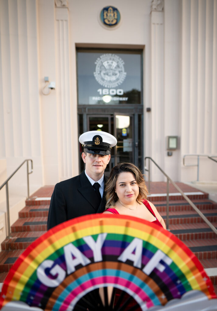 Couple at San Diego Courthouse holding up rainbow pride flag that says Gay AF