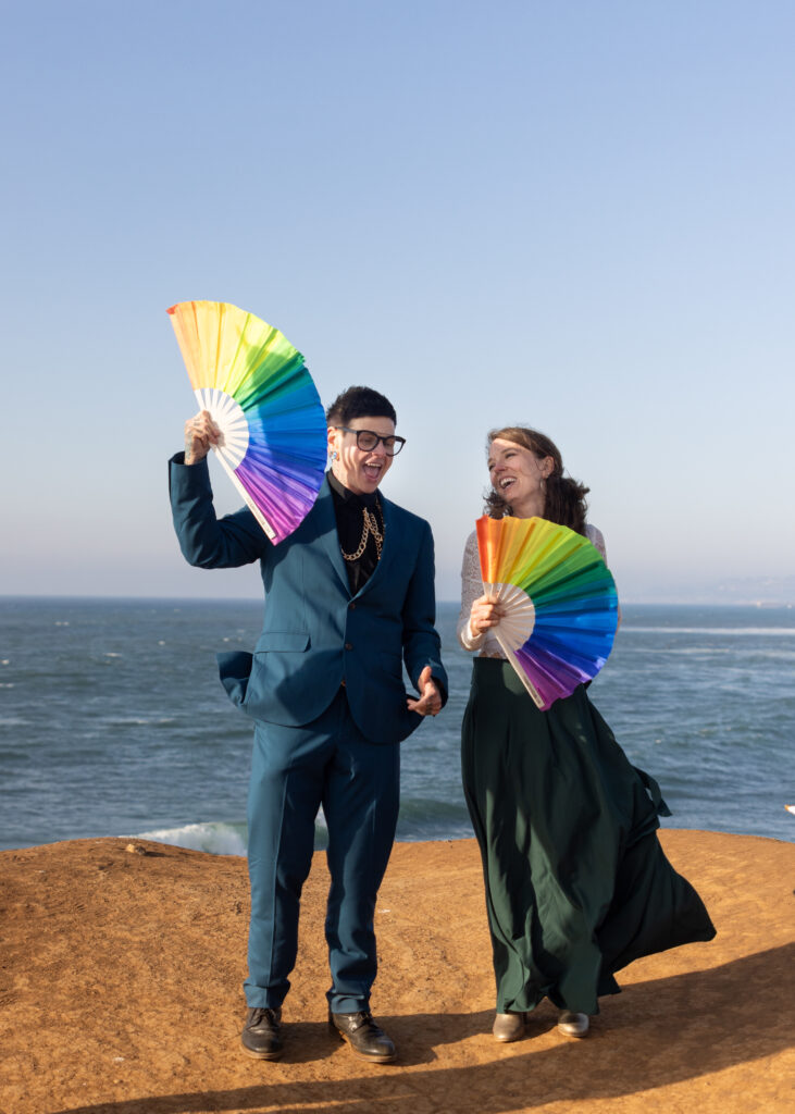 LGBTQ+ couples holds up pride flag at Sunset Cliffs wedding in San Diego
