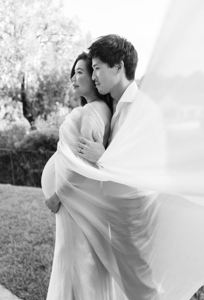 Couple stands together for a hug from behind at home for maternity session